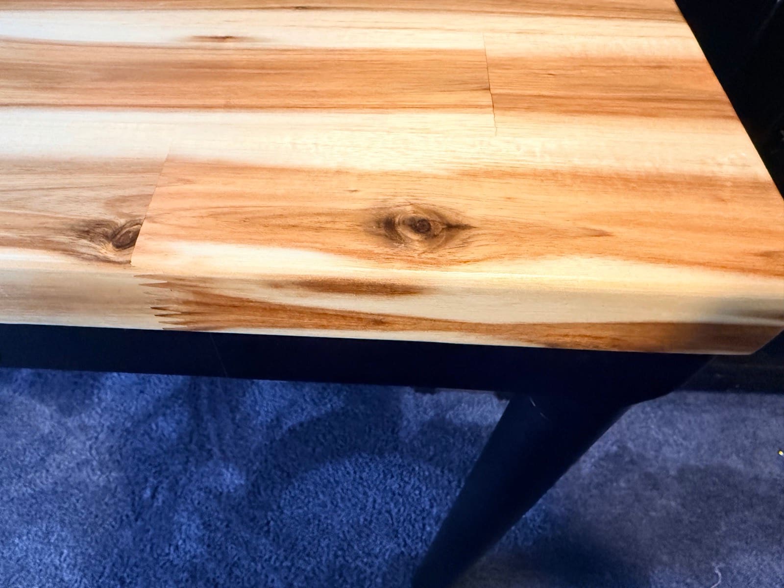 Close-up of the Acacia butcher block desktop after five weeks of daily use, showing the wood grain pattern with knots and mineral streaks, no scratches or wear marks visible