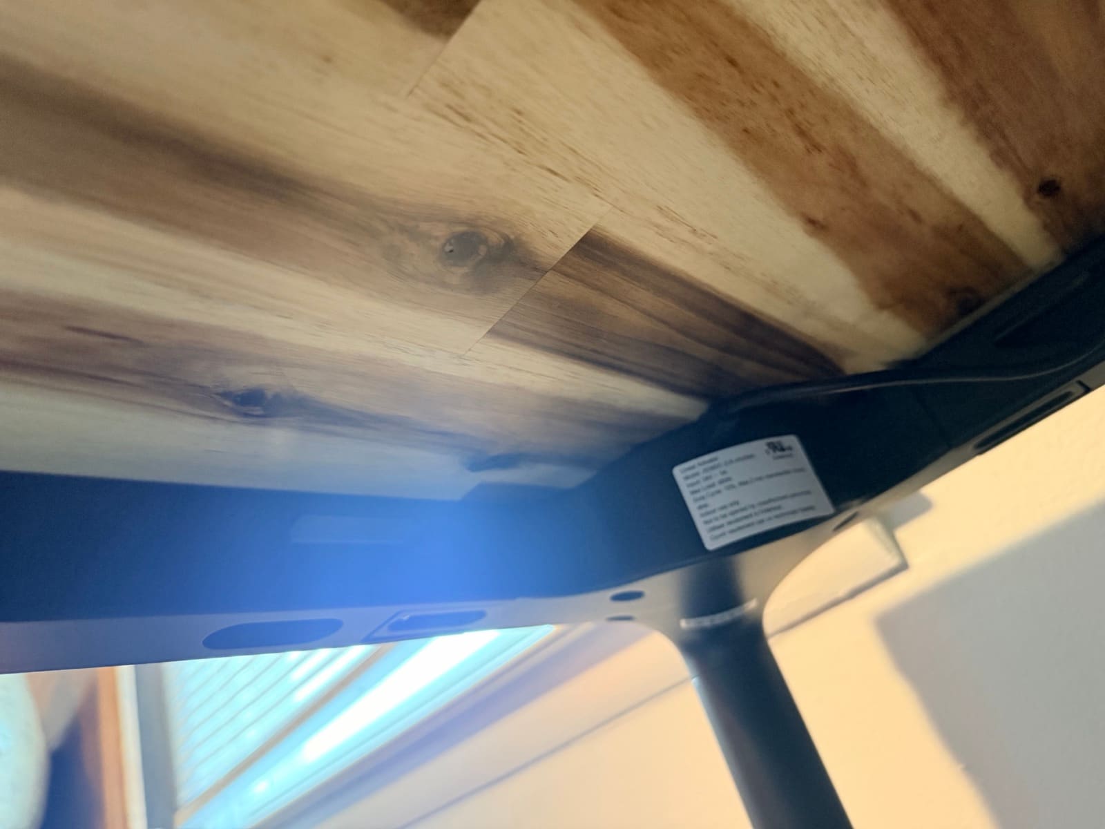 Under-desk view of the Parsons showing the control box, UL safety label, cable channel, and tapered leg meeting the underside of the Acacia butcher block