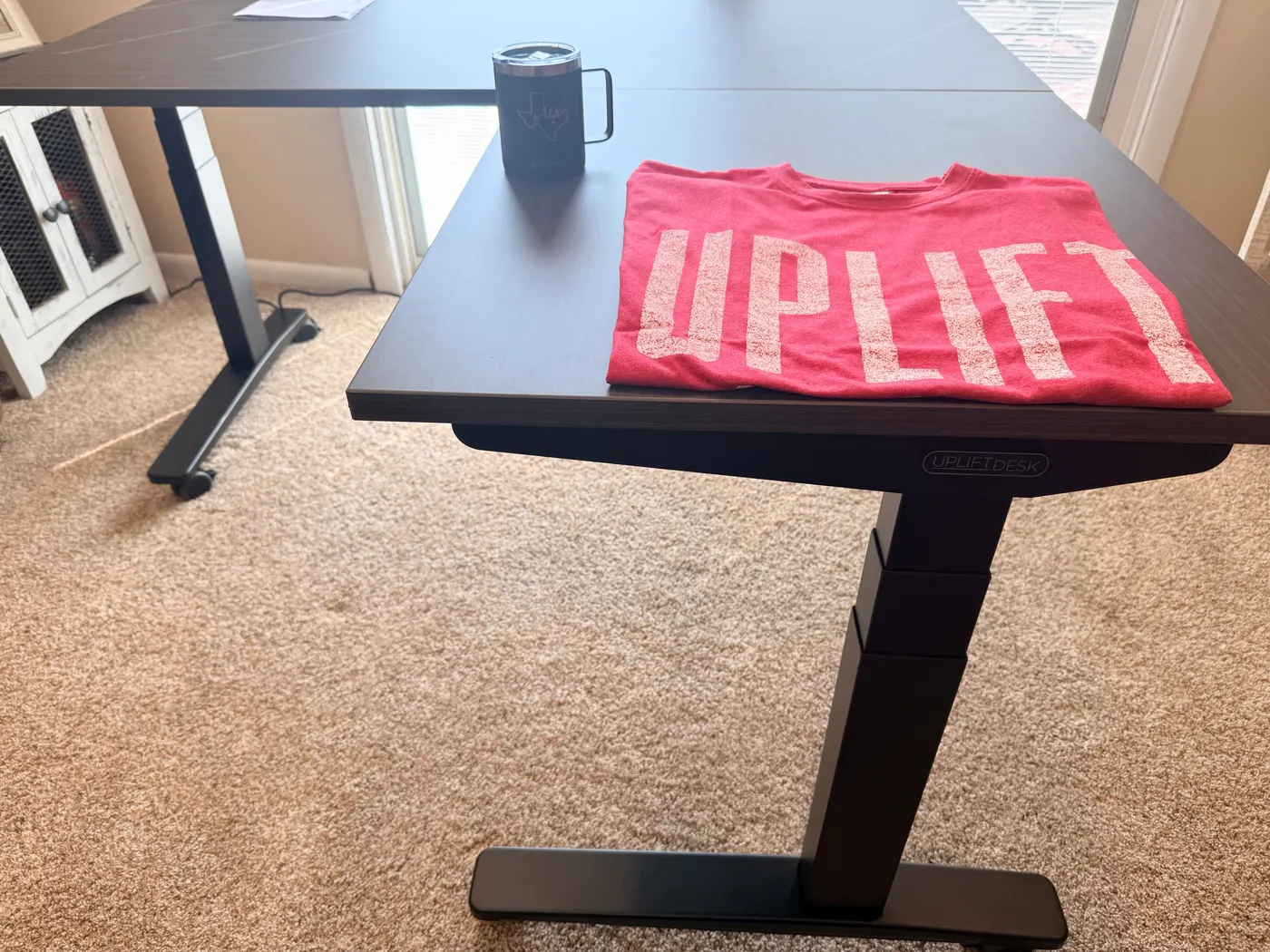The fully assembled UPLIFT V3 L-Shaped Standing Desk in Ash Gray laminate with the UPLIFT-branded Texas mug and pink Austin t-shirt that ship with the order
