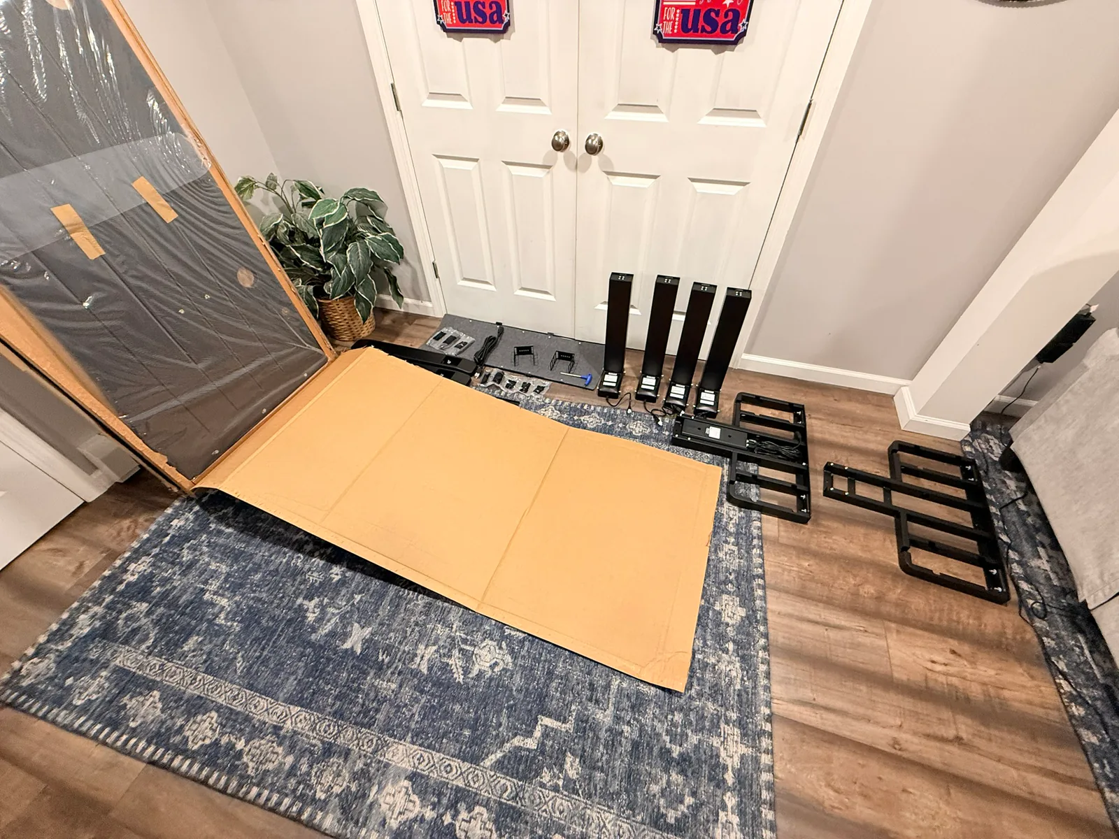 Four UPLIFT lifting columns, feet, rails, control parts, and the wrapped desktop laid out before assembly