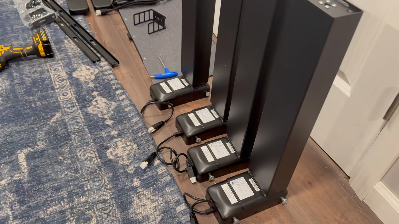 Four black UPLIFT lifting columns and motor housings lined up beside the desktop before installation