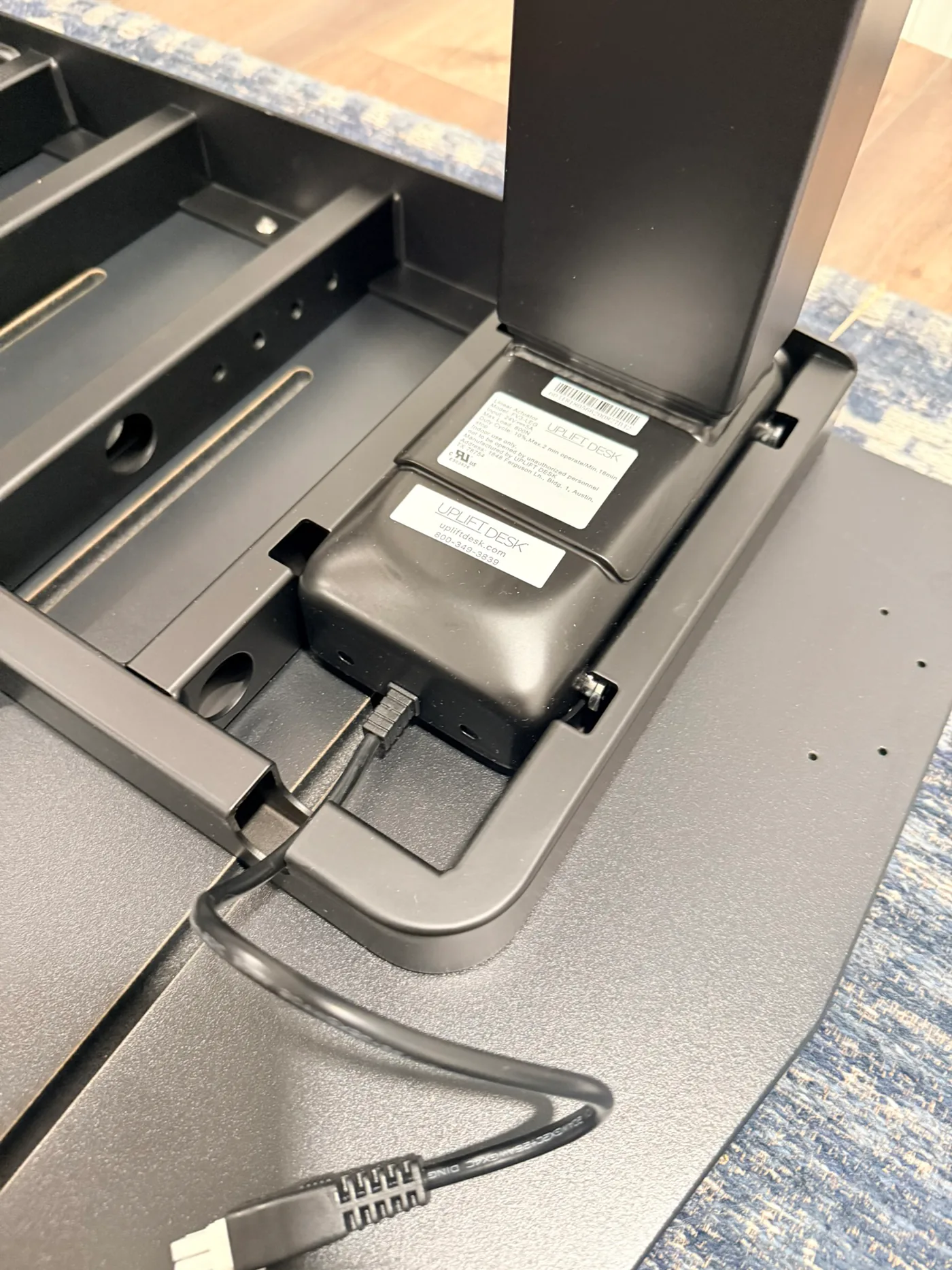 Black UPLIFT lifting column seated inside the frame corner receiver with its motor cable visible
