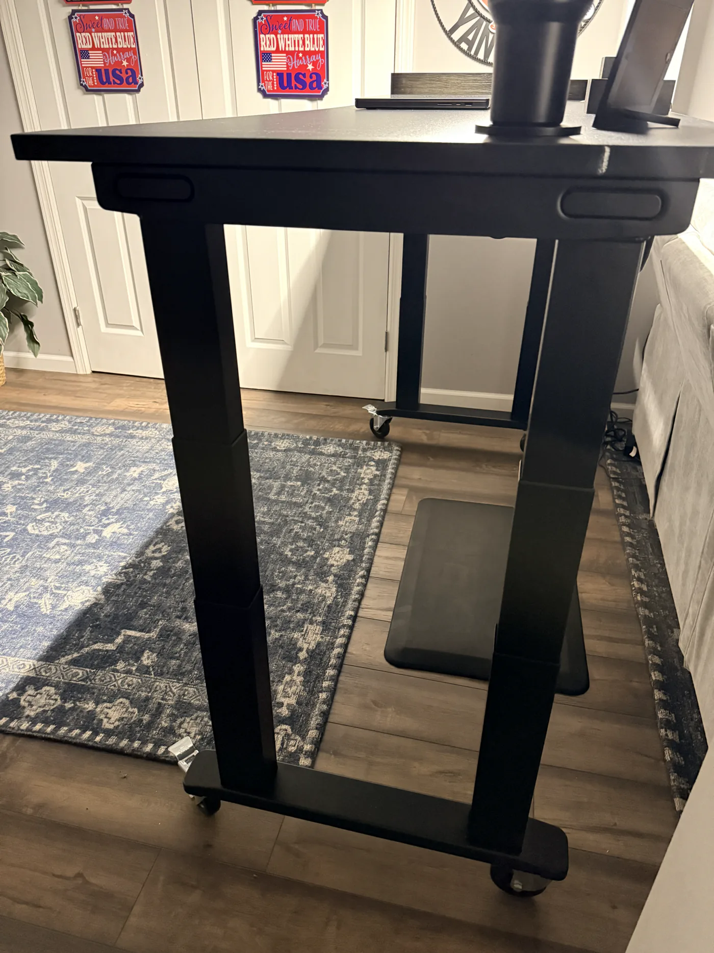 Raised black UPLIFT V3 4-Leg frame showing four telescoping columns and locking casters